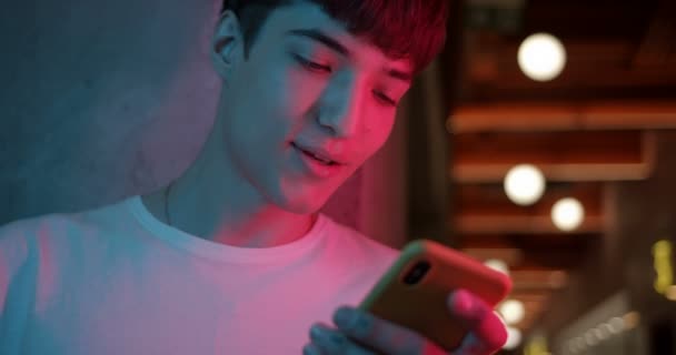 Close-up Shot van de jonge stijlvolle Millenial Boy Met behulp van zijn Smartphone, Lachen en Zeggen Wow, terwijl Staande bij Futuristische Neon Club Lights Achtergrond. Communicatieconcept. — Stockvideo