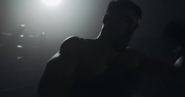 Siluet boksör adam karanlık spor salonunda kum torbası vurur. Yakın savaşçı egzersiz. Erkek boksör karanlıkta egzersiz. Kickboxer siluet eğitimi.