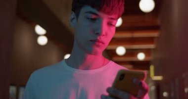 Beyaz tişörtlü, akıllı telefonuyla Fütürist Neon Kulüp Işıkları Arkaplanındaki Ekranda Yürüyen Adam tişörtünü giyen genç adam. Teknoloji Konsepti. Kapat..