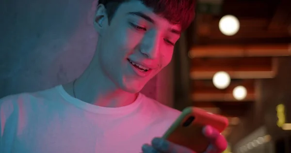 Close Up Shot of Young Stylish Millenial Boy Pomocí svého chytrého telefonu, Usmívající se a Saying Wow, zatímco stojí na pozadí Futuristic Neon Club Světla. Koncept komunikace. — Stock fotografie