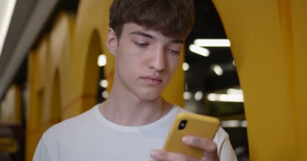 Close Up Shot of Young Cool Stylish Guy Wearing Using his Smartphone, Standing at Futuristic Yelow Walls and Lights at the Background. Communication and Technology Concept. — Stock Video