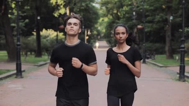 公園で走るジョギングスーツを着た若い白人男性とムスリンの女の子が笑顔でお互いにコンセプト｜健康的なライフスタイル. — ストック動画