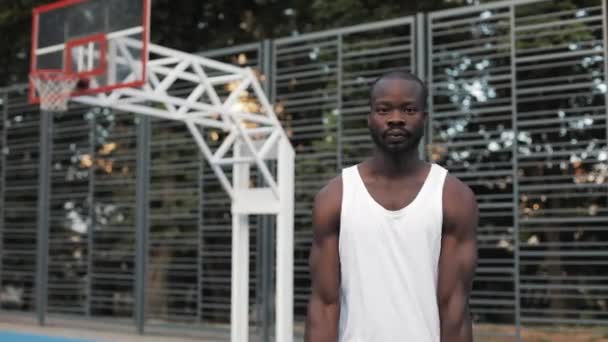 Portrét Muscly Handsome Afro - Americký chlap v bílém Singlet Dribling míč stojící na Street Basketbal sportovní hřiště a při pohledu na kameru. Zdravý životní styl a sportovní koncepce. — Stock video