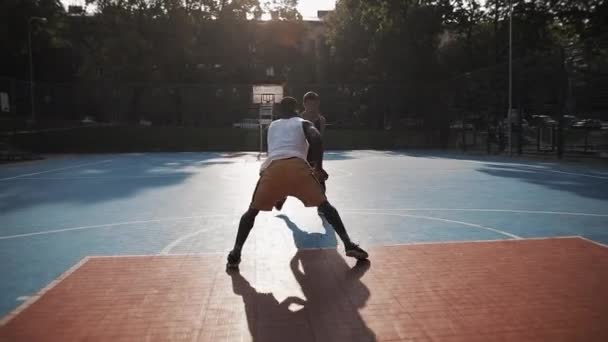 Dos jóvenes de raza mixta activa jugando baloncesto, pelota rebotando, uno a uno fuera en la cancha de baloncesto de deportes urbanos. Vida Saludable y Concepto Deportivo. Moción lenta . — Vídeos de Stock