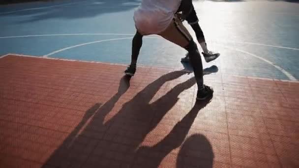 Low-Kamera-Blick auf zwei Sportler haben ein Basketballspiel, hüpfenden Ball, eins zu eins draußen auf dem städtischen Sport-Basketballplatz. gesunder Lebensstil und Sportkonzept. — Stockvideo