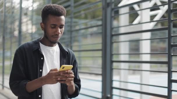 Chico joven escribiendo sms en el teléfono inteligente mientras camina . — Vídeos de Stock