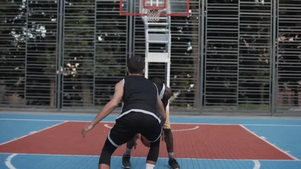 Due giovani giocatori di basket misti che giocano a basket uno contro uno, schivando sul campo da basket sportivo di strada. Spirito di competizione. Stile di vita sano e concetto di sport . — Video Stock