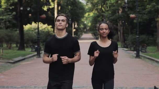 Молодой кавказский мужчина и девушка-муслин в беговых костюмах, бегающих в парке, улыбаясь концепции здорового образа жизни . — стоковое видео
