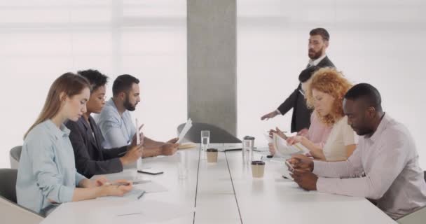 Snygg manlig chef som går in i konferenssalen och börjar arbeta möte. Multietnisk grupp av kontorsanställda som sitter och har information om arbetet. Begreppet arbete, internationalitet. — Stockvideo