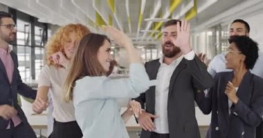 Yaratıcı ekibin başarılı bir iş sunumundan sonra eğlenmesine yakın durun. Genç enerjik çalışanlar dans ediyor, beşlik çakıyor ve kârlı bir anlaşma imzaladıktan sonra gülümsüyor. Zafer kavramı.