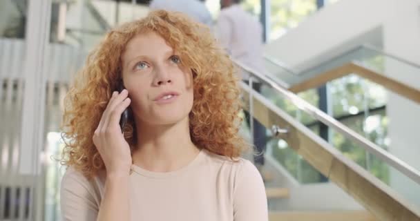 Gros plan d'une jolie employée de bureau debout et communiquant par téléphone mobile. Jeune femme d'affaires aux cheveux bouclés ayant parlé sur son smartphone. Personnes et communication . — Video