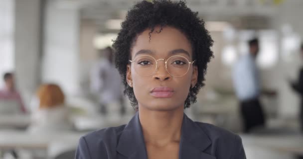Közelkép magabiztos vegyes verseny női főnök nézi a kamera. Vonzó fiatal nő szemüvegben a modern irodai munkaterületen. Emberek portréi. Homályos háttér. A karrier fogalma. — Stock videók