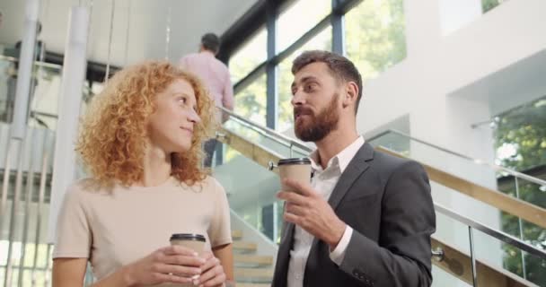男性と女性のオフィススタッフが立って会話をし、休憩中にコーヒーを飲んでいます。起業家が話して笑顔で、自由な時間でプロジェクトを議論する。コミュニケーションの概念. — ストック動画