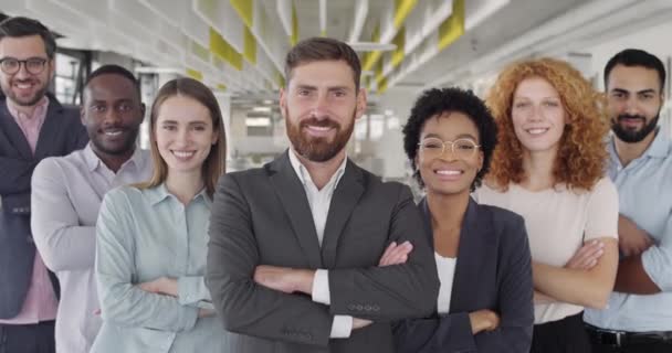 Portret van een lachend zakenteam dat camera 's kijkt en elkaars handen kruist. Bekijk van dichtbij de positieve groep van diverse collega 's die glimlachen en staan in het moderne zakencentrum. Concept van teamwork. — Stockvideo