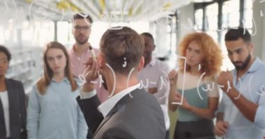 Yakışıklı girişimci, iş arkadaşlarıyla cam bir tahtada iş fikirlerini ve planlarını tartışıyor. Erkek ofis çalışanı cam duvardaki verileri açıklıyor ve iş arkadaşlarıyla konuşuyor..