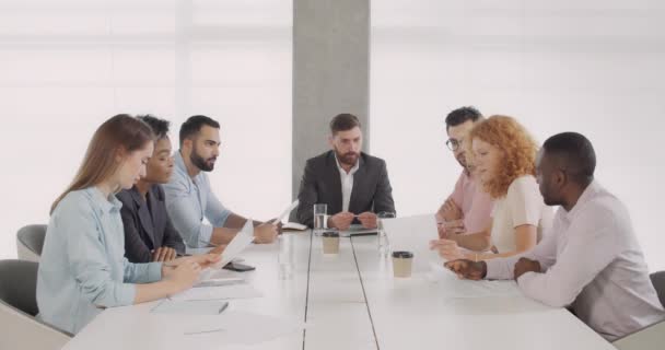Junge multiethnische Mitarbeiter eines Unternehmens, die sich in Unternehmen treffen. Eine Büroangestellte spricht und zeigt ihren Kollegen Dokumente, während sie am Konferenztisch sitzt. Konzept der Teamarbeit. — Stockvideo