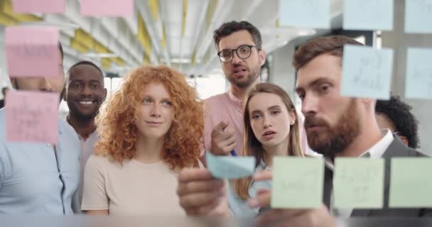 Közelkép a változatos irodai csapat férfi vezető ötletelés és stiking üvegtáblán. A női irodai dolgozó megtalálja a megfelelő megoldást, és pacsit ad a munkavezetőnek.. — Stock videók