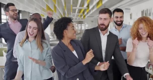 Coşkulu çok ırklı iş arkadaşları şirket zaferini kutluyor ve birlikte eğleniyorlar. Neşeli genç ofis çalışanları dans ediyor, gülümsüyor ve hareket ediyor, kutluyor. İnsan kavramı, olumlu duygular.. — Stok video