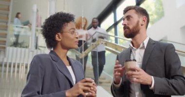 Kadın ve erkek ofis çalışanları sohbet ediyor ve kahve fincanlarıyla ayakta duruyorlar. Çeşitli etnik kökenden iş arkadaşları boş zamanlarında ofis salonunda sohbet edip gülümsüyorlar..