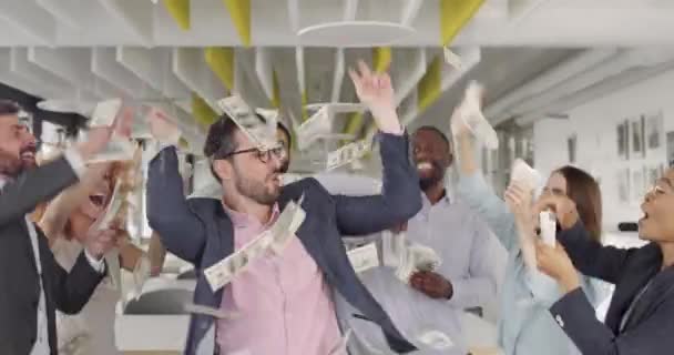 Gruppe von Bankangestellten, die sich amüsieren und mit Geld werfen, während sie sich über gute Geschäfte freuen. fröhliche junge Mitarbeiter tanzen und feiern große Gewinne in modernen Büroarbeitsplätzen. — Stockvideo