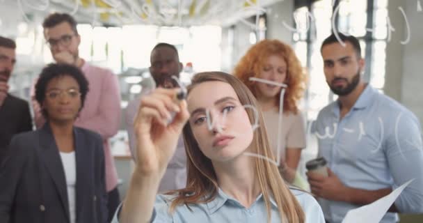 Diverse group of finance office worker having corporate training and using glass board.Young woman ofice worker standing and writing on glass wall an talking with her colleagues. — Stock Video