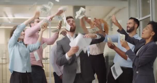 Employés de bureau masculins et féminins dansant avec de l'argent et des documents à l'espace ouvert.Équipe d'affaires excitée jetant des billets de banque et des papiers en dollars dans le bureau. Concept d'entreprise prospère .