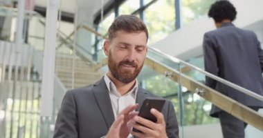 Akıllı telefon kullanan ve modern ofiste duran sakallı işadamlarına yakın çekim. Erkek şirket şefi internette sörf yapıyor ve cep telefonunu araklıyordu. İnsan kavramı, iş, teknoloji.