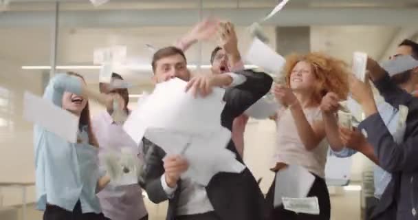 Male and female office team celebrating successful meeting. Happy employees throwing up documents and banknotes while dancing in working space. Concept of success and good mood. — Stock Video