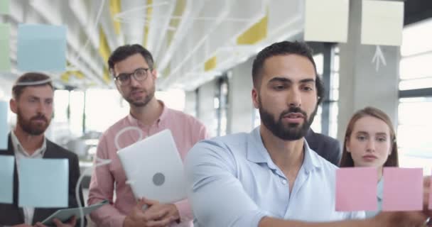 Retrato de belo empresário barbudo escrevendo em placa de vidro. executivo Ceo explicando estratégia de negócios para seu colega no quarto de escritório moderno. Conceito de criatividade e trabalho em equipe . — Vídeo de Stock