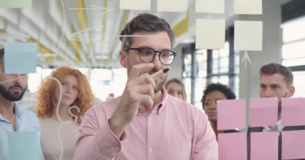 Ein männlicher Büroangestellter in Brille denkt nach und zeigt seinen Kollegen neue Problemlösungen. gutaussehender Teamleiter, der seine Idee mit Bürokameraden teilt und Glasplatten verwendet. Konzept der Kreativität. — Stockvideo