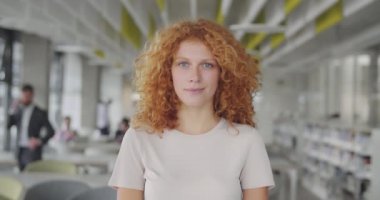 Modern ofis çalışma alanında duran kıvırcık saçlı yöneticinin ön görüntüsü. Çekici, gülümseyen genç bir bayanın portresi.