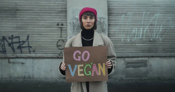 Elinde Go vegan tabelası olan genç bir kız boş caddede kameraya bakıyor. Kadın hipster vejetaryenliği ve sağlıklı yaşam tarzını destekliyor. Go Green Go Vegan ve Eko Konsepti.