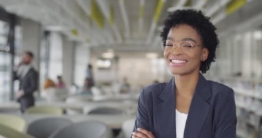 Takım elbiseli başarılı bir iş kadını gülümseyip kameraya doğru dönüyor. Modern ofiste duran Afro-Amerikan kadın ofis çalışanı. Portreler