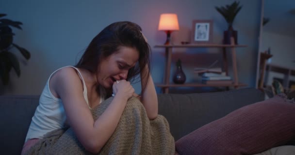 Eenzaam verdrietig meisje zittend op de bank in foetale positie en huilend. Depressieve jonge vrouw in tranen bedekt met deken brak met vriendje. Begrip eenzaamheid en relatie. — Stockvideo