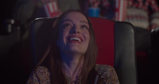 Sluiten van gelukkig mooi meisje gezicht kijken comedy film in de bioscoop. Millennial vrouw zit in stoel en lachen in de bioscoop. Concept van entertainment. Positieve emoties. — Stockvideo