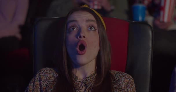 Close-up van Millennial vrouw zitten in stoel en reageren in ontzag voor spannende moment in de film. Mooi meisje kijken film in de bioscoop met geopende mond en grote ogen. Amusement. — Stockvideo