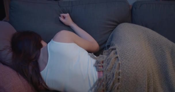 用她的手拍沙发枕头的背景。年轻的女人躺在沙发上，盖着毛毯，看起来很不高兴，很生气。家庭背景. — 图库视频影像