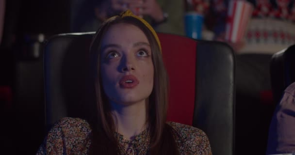 Close up of pretty girl face watching action film in cinema. Young woman sitting in chair, holding breath and making big eyes in movie theatre. Concept of entertainment and people emotions. — Stock Video