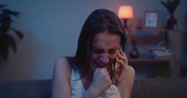 Akıllı telefondan konuşurken ağlayan ve selamlaşan üzgün kızı kapat. Mutsuz bir kadın, telefon görüşmesi sırasında koltukta otururken kötü haberlere inanamaz. Duygusal konuşma kavramı.