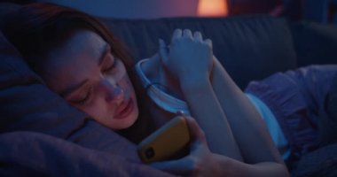 Kanepede uzanan ve gece akıllı telefon kullanan yalnız genç bayanı yakından çek. Depresyondaki bin yıllık kadın cep telefonu ekranına bakıyor ve düşünüyor. Acı verici ayrılık kavramı.