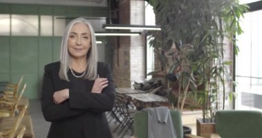 Orta yaşlı bir iş kadınının elleri çapraz duruşu. Takım elbiseli çekici kadın girişimci kameraya bakıp gülümsüyor. Portreler. Modern ofis geçmişi.