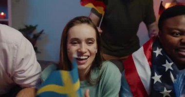 Bayrakları olan, TV 'de spor izleyen ve kanepede oturan çok ırklı insanlara yakın durun. Elinde İsveç bayrağı ve gülümseyen ve şarkı söyleyen piliçlere odaklan..