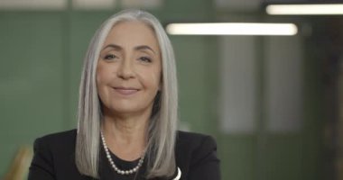 Close up of good looking middle aged businesswoman looking to camera and smiling while standing in office. Portraits. Blurred background. Concept of business and success.