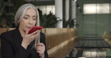 Kafede otururken akıllı telefon kumandanı kullanan olgun bir kadına yaklaş. Eski modern iş kadını iş arkadaşına sesli mesaj yazdırıyor. İnsan ve teknoloji kavramı.