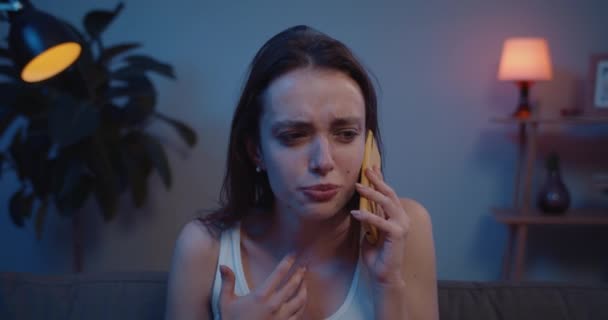 Close-up van jonge geïrriteerde vrouw praten op smartphone en ruzie maken. Millennial meisje met rommelige mascara op haar gezicht met emotionele gesprek terwijl zitten op de bank thuis. — Stockvideo