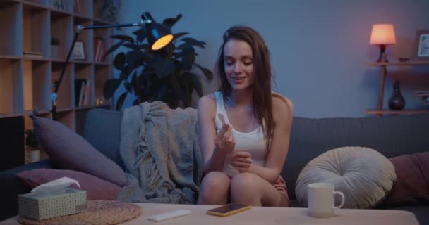 Kanepede otururken hamilelik testi tutan mutlu kız. Genç bir kadın testçide pozitif sonuç için heyecanlanıyor. Olumlu duygular kavramı. Arka plan.. — Stok video