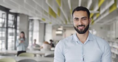 Gömlekli yakışıklı patron başını kameraya çeviriyor ve gülümsüyor. Genç erkek ofis çalışanı mutlu görünüyor ve modern ofis çalışma alanında duruyor. Portreler. Bulanık arkaplan.