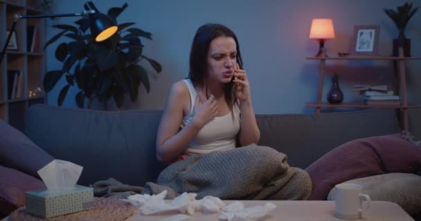 Front view of young annoyed woman sitting while having quarrel and talking on mobilephone . Annoyed woman finishing phone conversation and throwing her smartphone angrily on sofa. — Stock Video