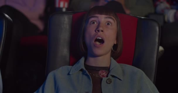 Hipsterka ogląda film akcji w kinie. Młoda kobieta robi wielkie oczy, otwiera usta i mówi "wow" w kinie. Pojęcie rozrywki i emocji ludzi. — Wideo stockowe