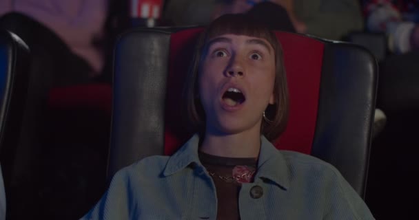 Hipster cara chica viendo película de acción en el cine. Mujer joven haciendo grandes ojos, boca abierta y diciendo wow en el cine. Concepto de entretenimiento y emociones de la gente . — Vídeos de Stock